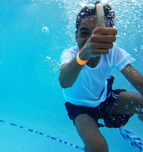 Child swimming underwater and giving a thumbs-up during a summer swim lesson.