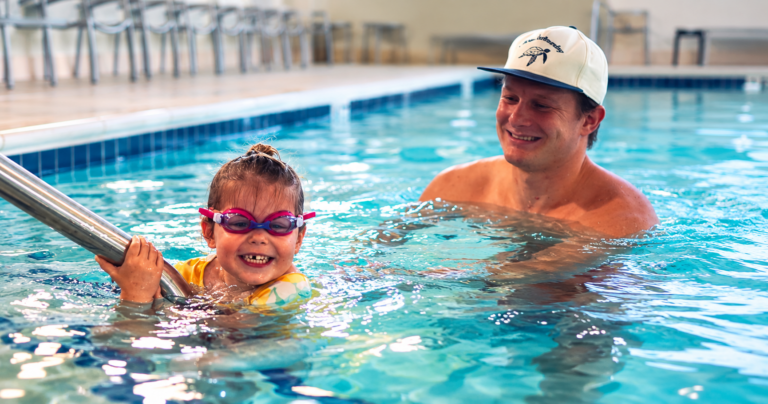 Child smiling in a swimming pool with a Swim & Play instructor during a swim lesson in Nashville.